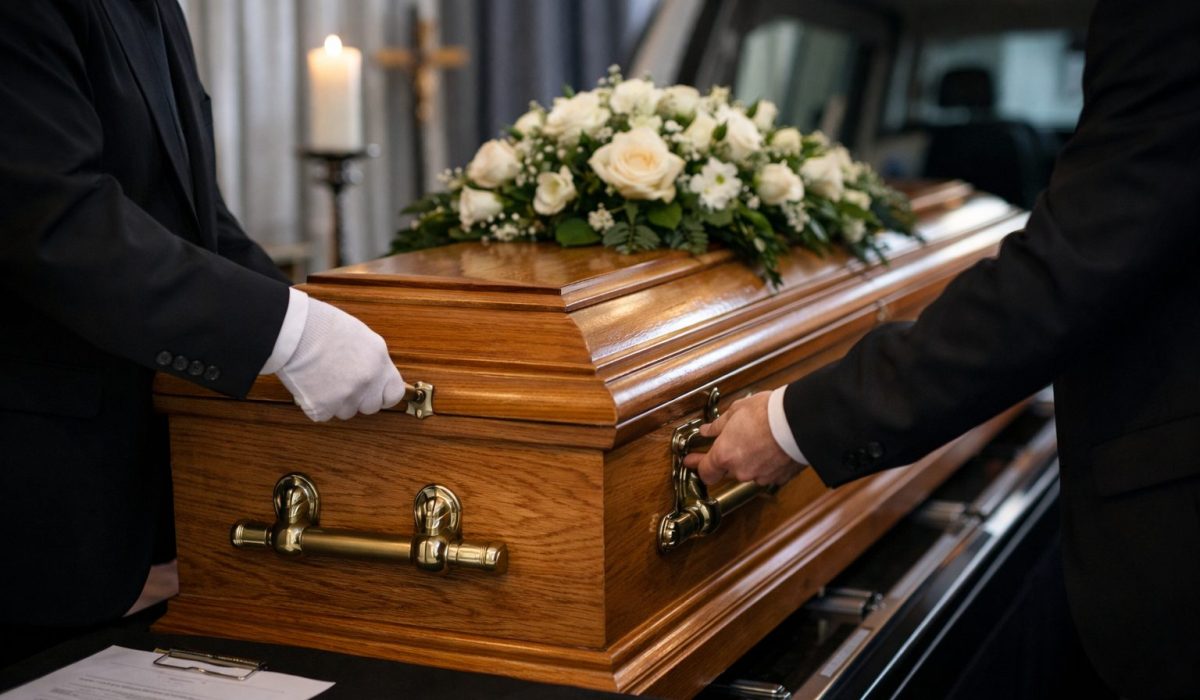 Deux agents funéraires ferment un cercueil en bois verni avec une gerbe de fleurs blanches, dans une chambre funéraire, avant le départ du corbillard.